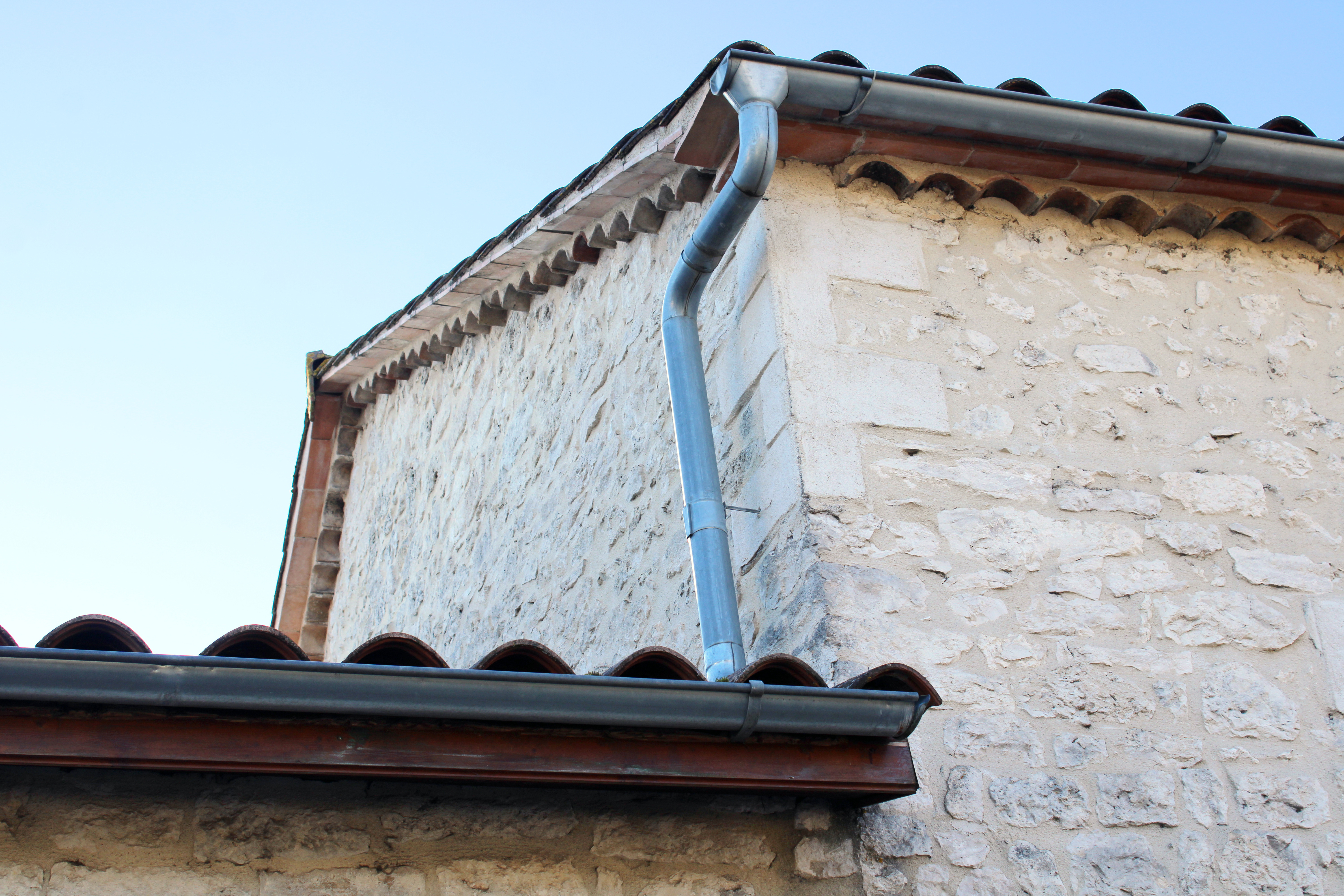 Gouttière zinc gris sur la façade de la maison, descentes rondes sur la façade en pierre